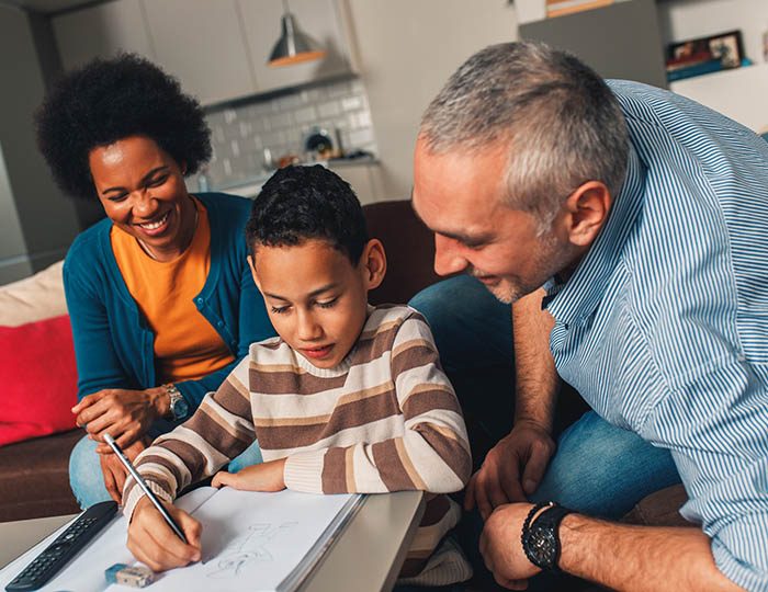 Parents helping their son with his homework at home in living ro